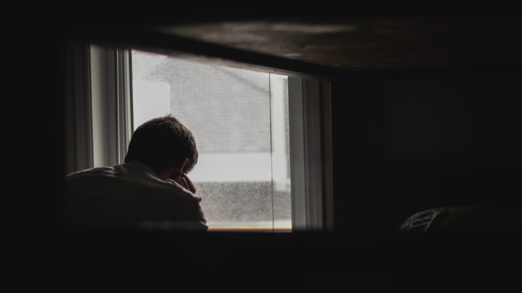 man sitting near window in dark room