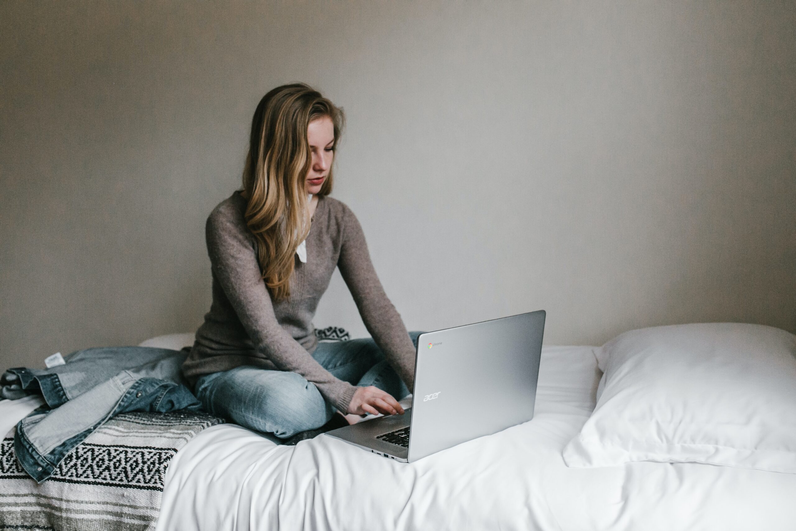 a young white blonde woman using a laptop while sat on a bed