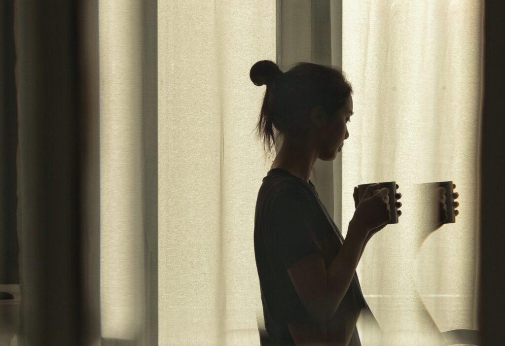 image of woman with a cup of tea looking out the window refracted through glass
