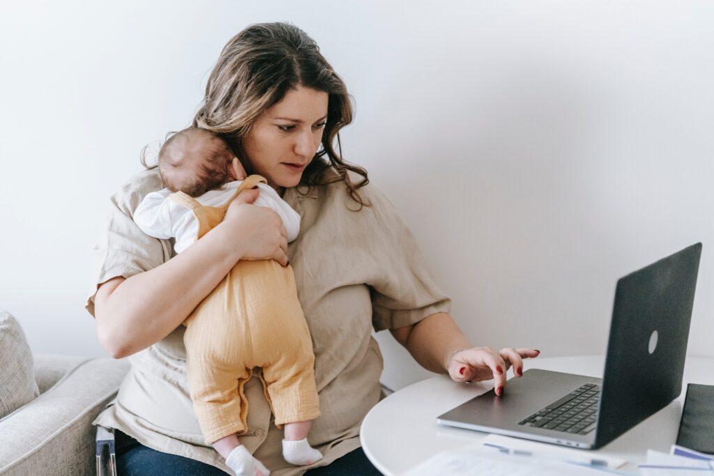 A mother clutches her sleeping baby as she uses a laptop