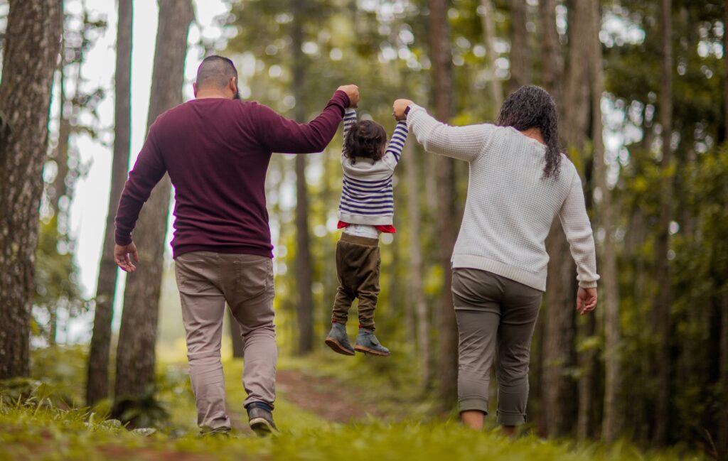Parents lifting their child by the hands on a walk in nature