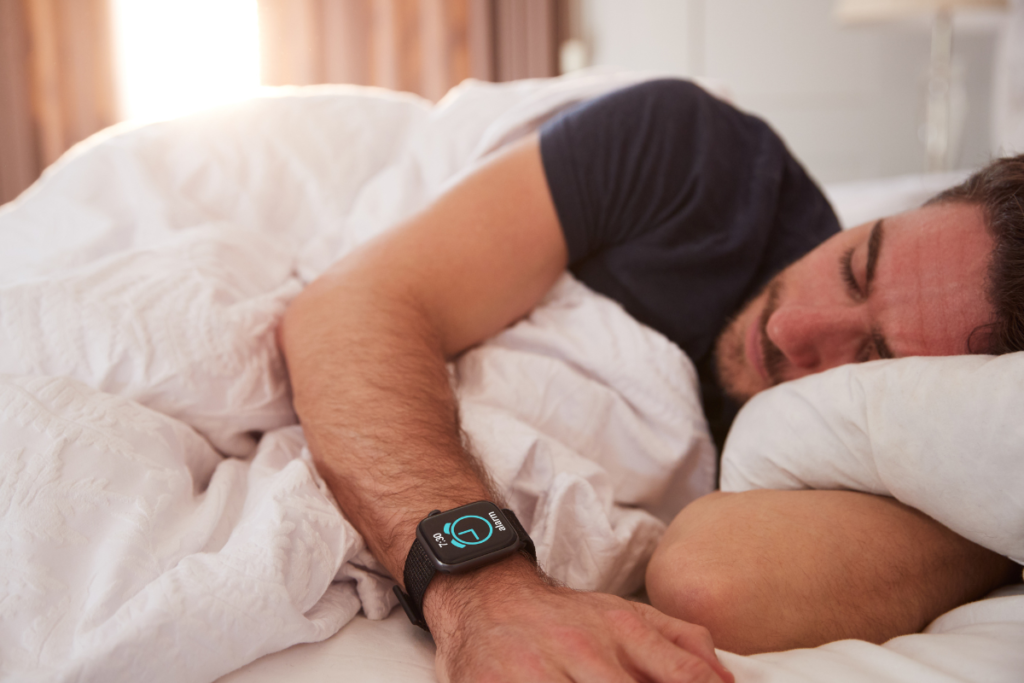 a young white man asleep in bed with a smart watch on his wrist