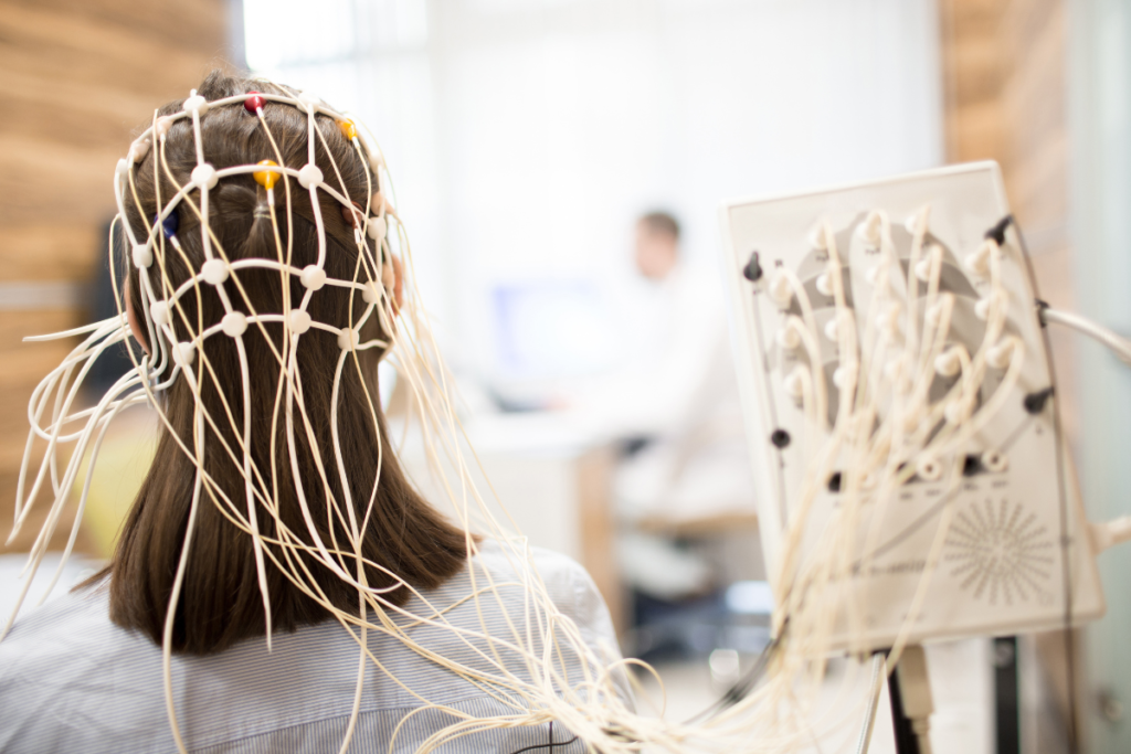 an eeg machine with lots of wire attached to a young woman's head with long brown hair