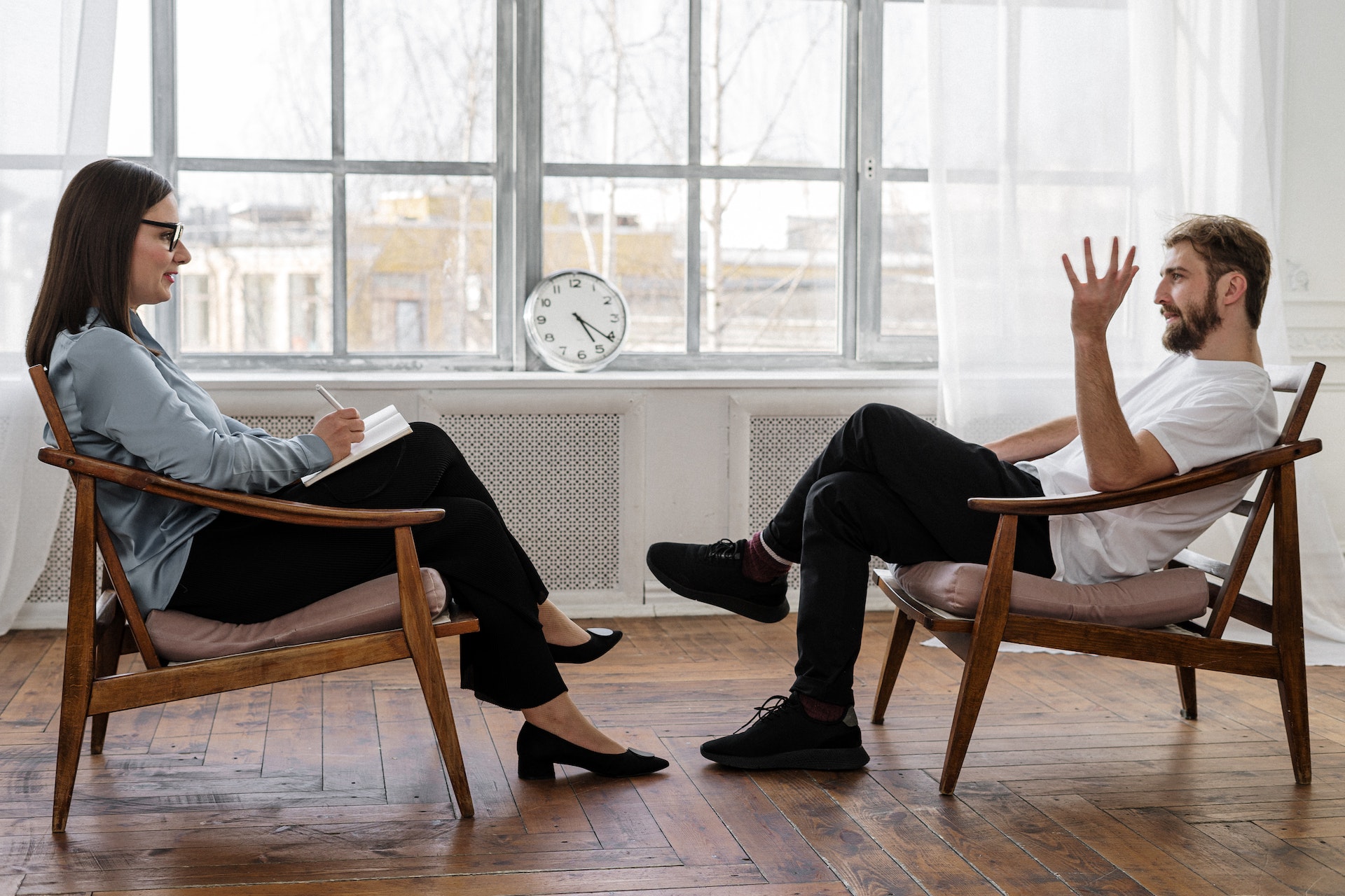 photo of a man and woman sitting on chairs in a bright room opposite each other to indicate that this may be a therapy session